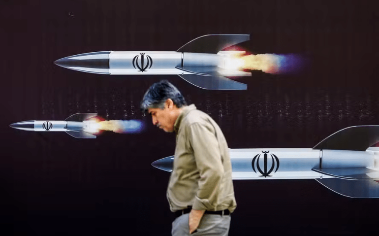 Homem passa em frente a banner com imagem de mísseis em Teerã — Foto: AFP