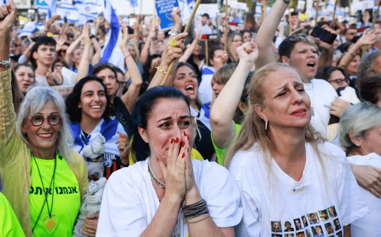 Uma mulher reage enquanto pessoas comemoram na Praça dos Reféns em Tel Aviv, após a divulgação da notícia de que um comboio da Cruz Vermelha está a caminho para resgatar um segundo grupo de reféns israelenses  que serão libertados pelo Hamas em 13 de outubro de 2025. (Menahem Kahana/AFP)