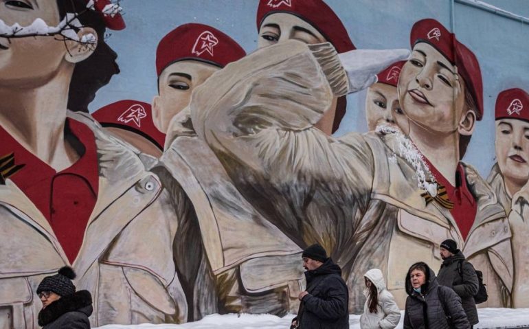 Pessoas passam diante de mural em homenagem à Yunarmiya, o Exército da Juventude, organização ligada ao Ministério da Defesa, em Moscou Foto: SERGEY PONOMAREV / NYT