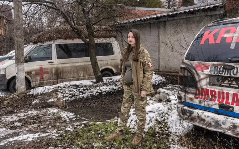 Olya, em Sloviansk, Ucrânia, em janeiro, não conseguia mais abotoar as calças e aguardava um uniforme de maternidade de Zemliachky. Médica de combate, ela disse que ia "com os rapazes para todas as posições de combate, para as trincheiras" em um Nissan Pathfinder coberto de lama, com as portas laterais abarrotadas de torniquetes e gloss labial no console central — Foto: Brendan Hoffman / The New York Times