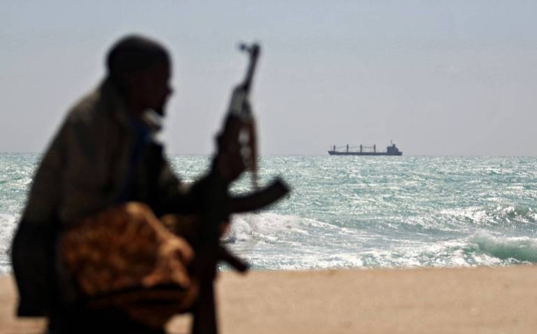 Pirata somali armado na costa do país africano, com um cargueiro grego ancorado ao fundo - Mohamed Dahir - 7.jan.2010/AFP
