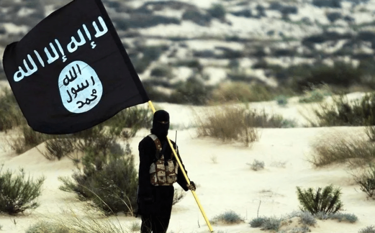 Soldado mascarado do Estado Islâmico posa segurando a bandeira em algum lugar nos desertos do Iraque ou da Síria  • History/Universal Images Group via Getty Images